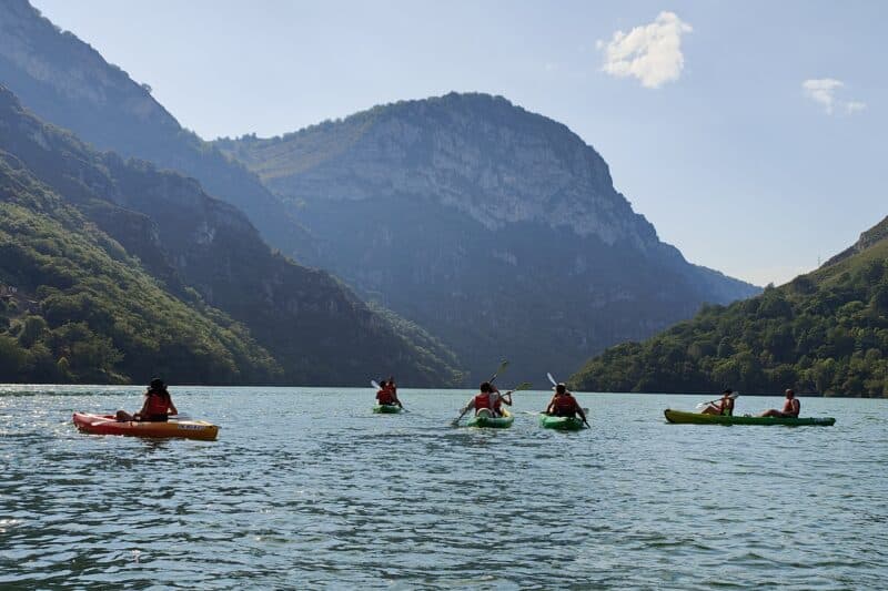 Gente en kayak en lago montañoso con sol brillante.