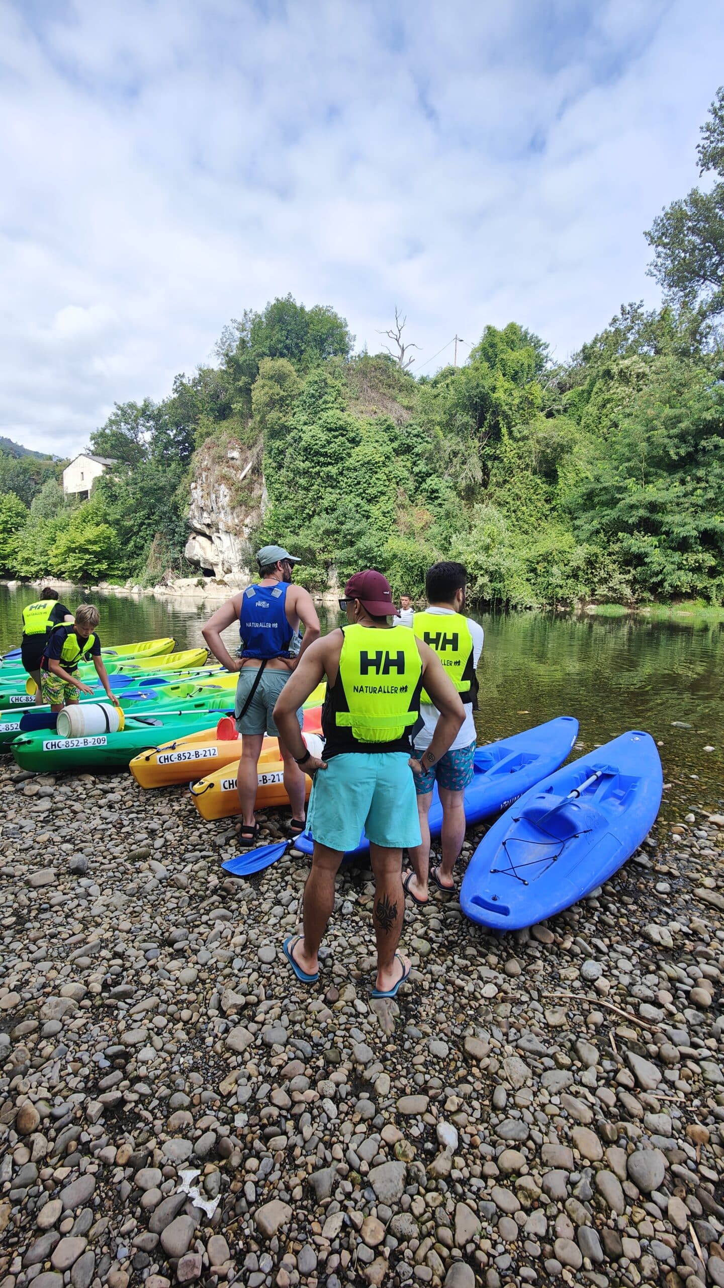 Grupo preparando kayaks junto a río arbolado.