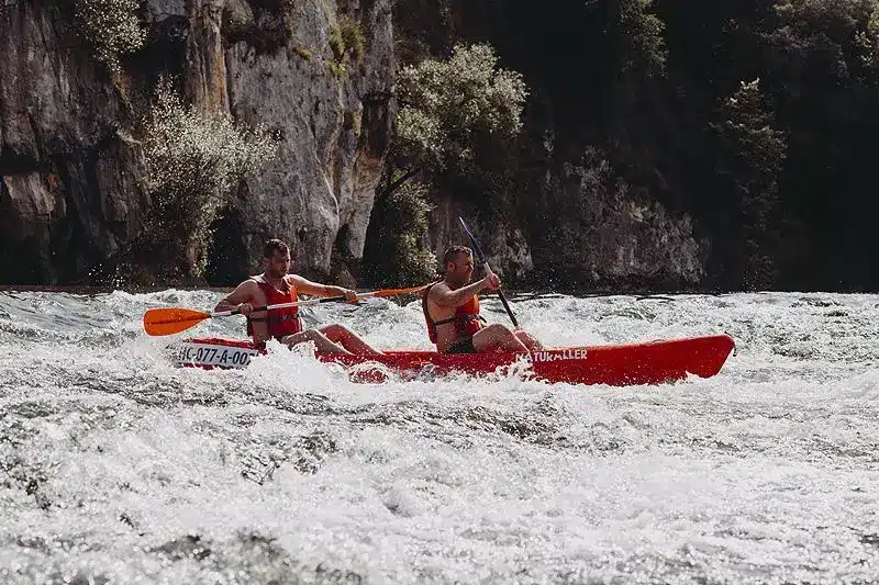 Dos personas remando en kayak en río turbulento.